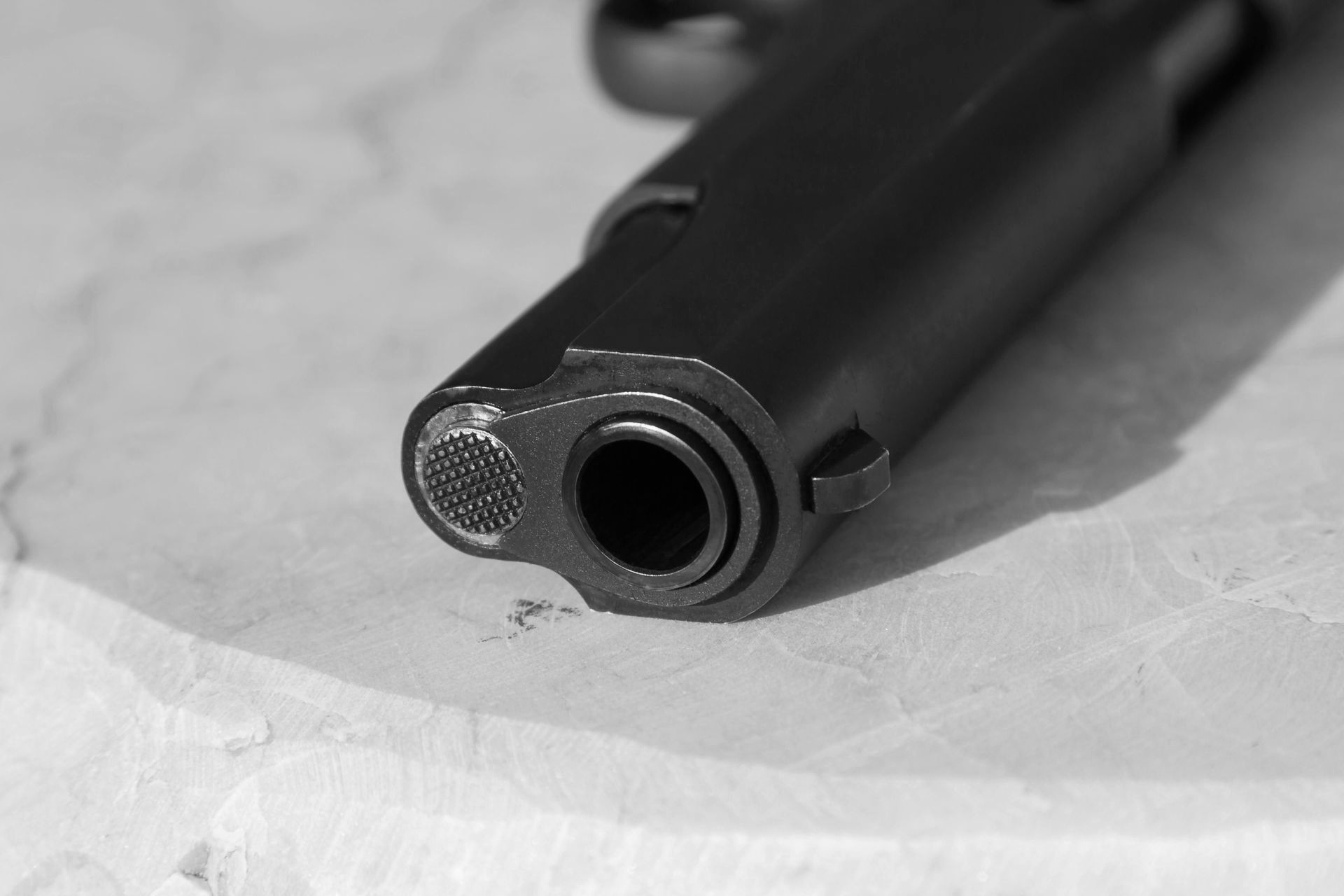 Close-up of a black handgun, barrel pointed forward on a textured surface.