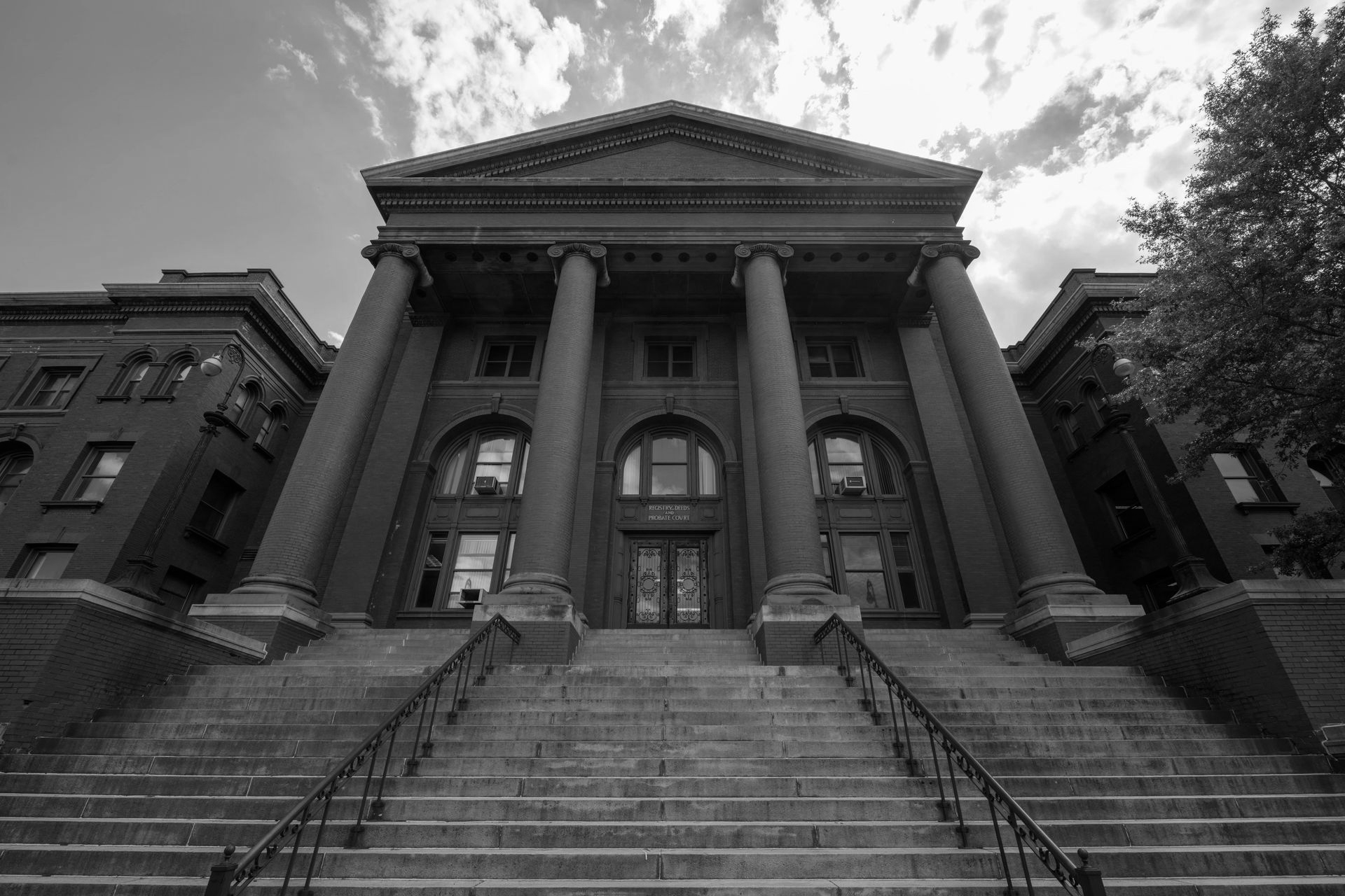 Grand, classical-style building with columns, steps leading up. Black and white photo.