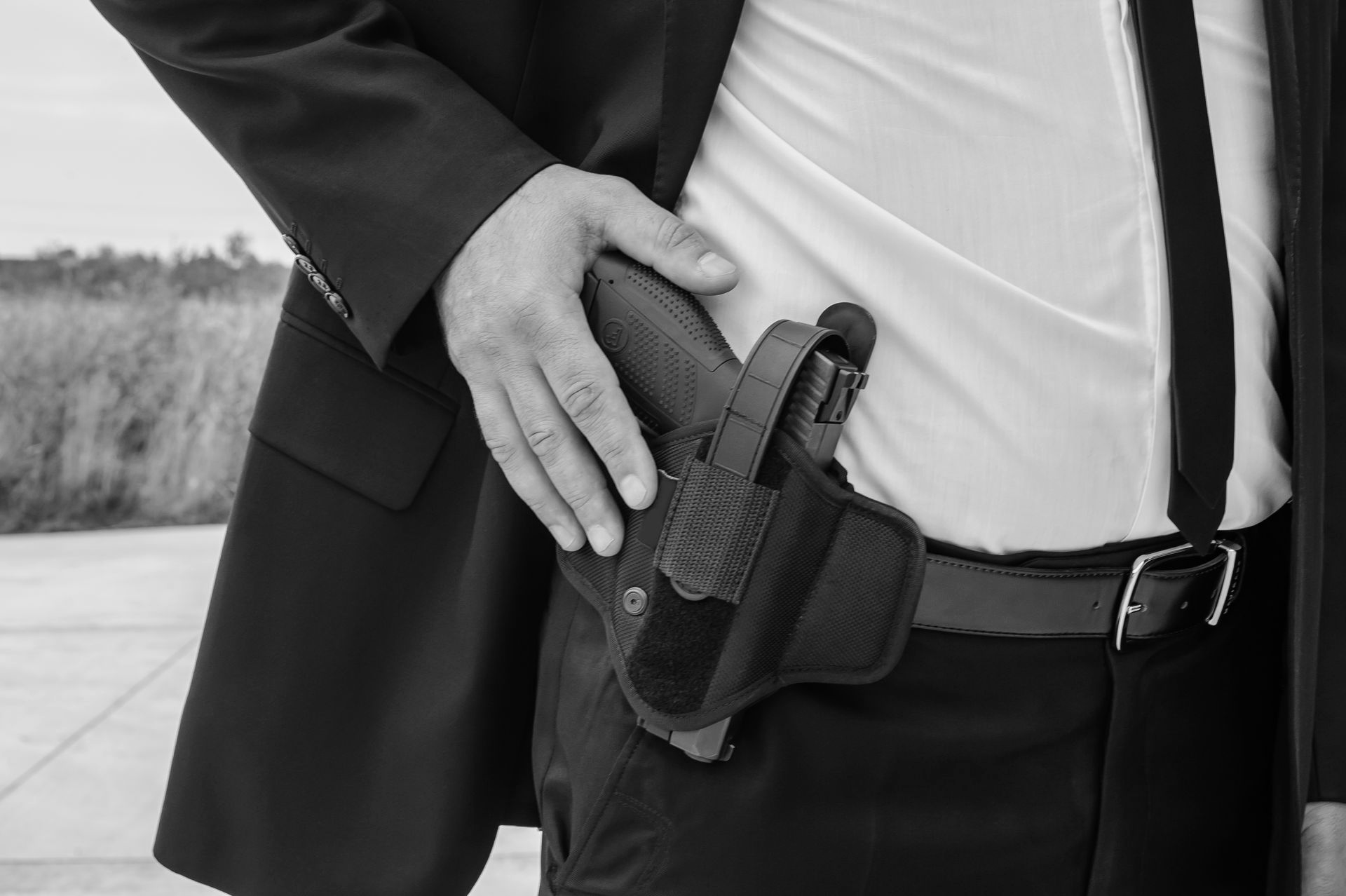 Man in suit, holding a gun in a holster at his waist.