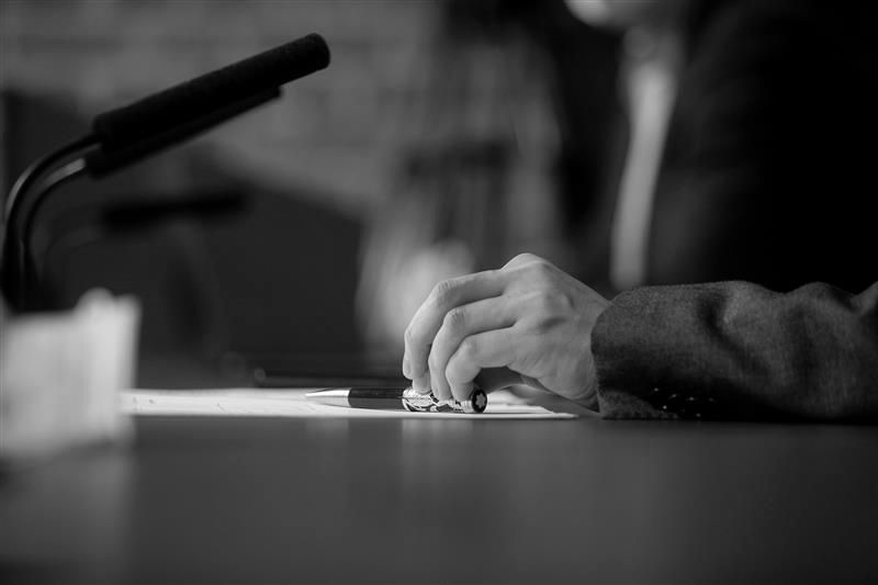 A person's hands on a table, with a pen in hand, in front of a microphone.
