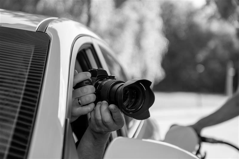 Photographer holding camera out of car window, taking a photo at gas station.