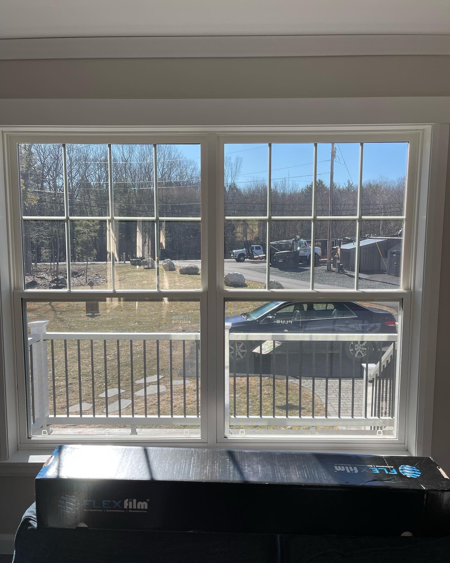Window view of a yard with cars, trees, and a house. A black box sits in front of the window.