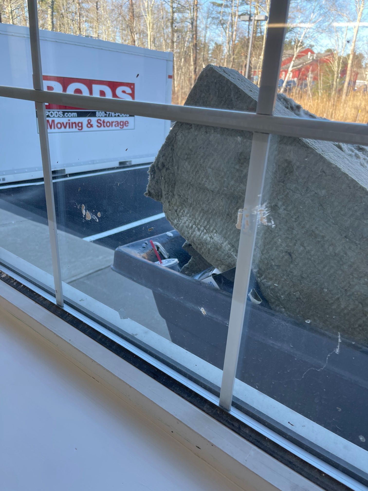View through window of a truck bed with a large, gray stone block; PODS moving container in the background.