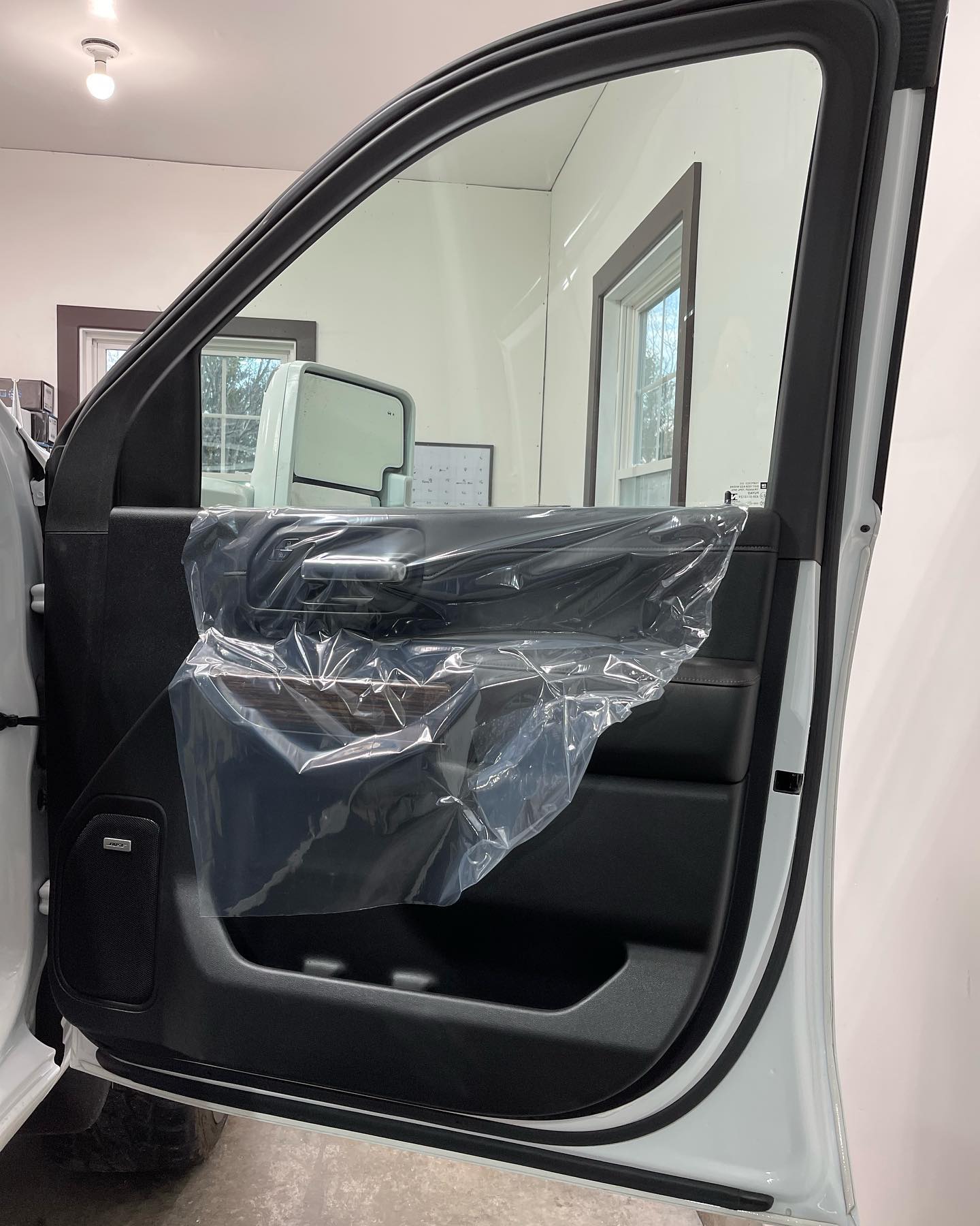Open white car door with clear plastic cover on the black interior. Interior and outside visible through the glass.
