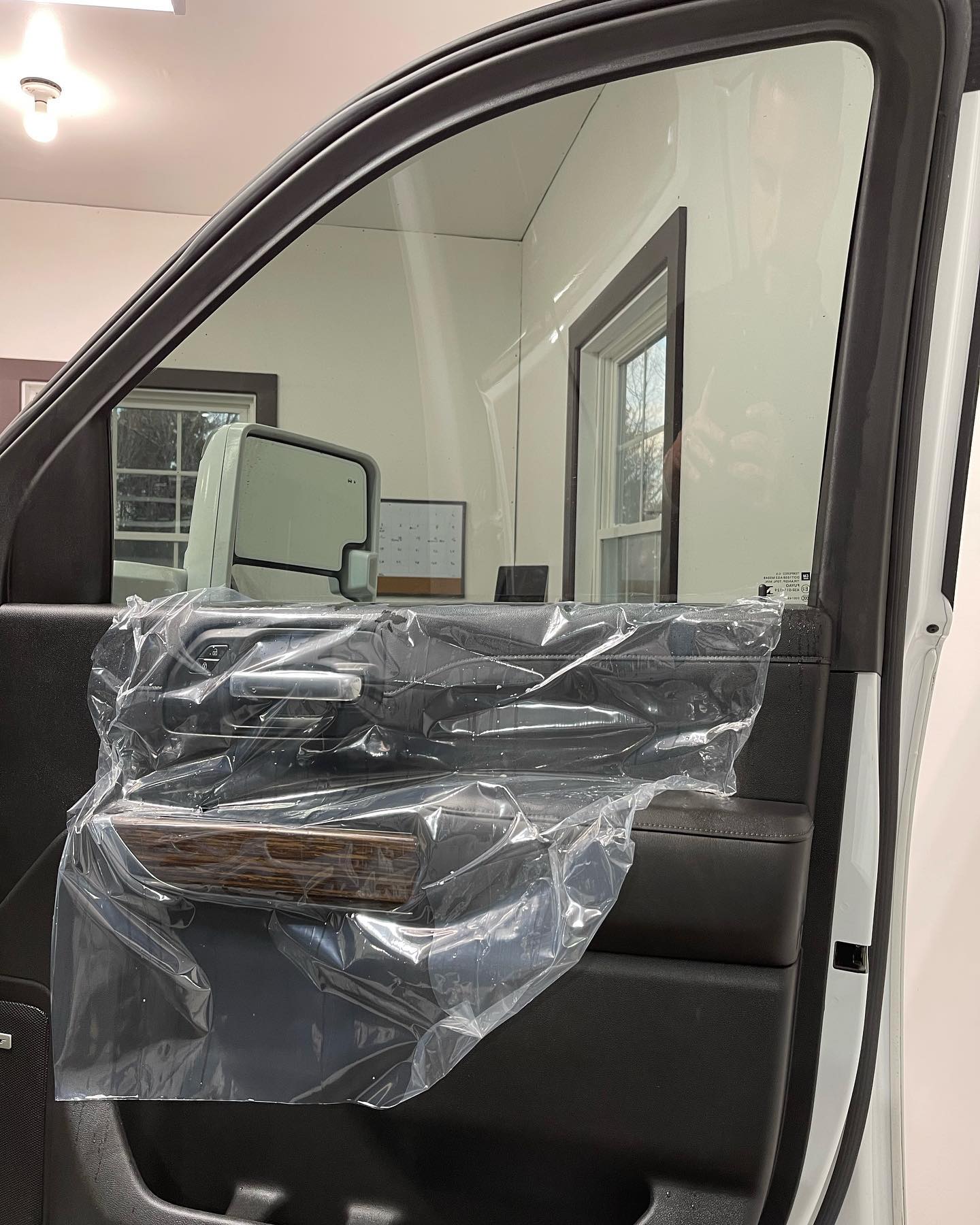 Car door interior with plastic wrap covering the armrest, revealing a bright office setting.