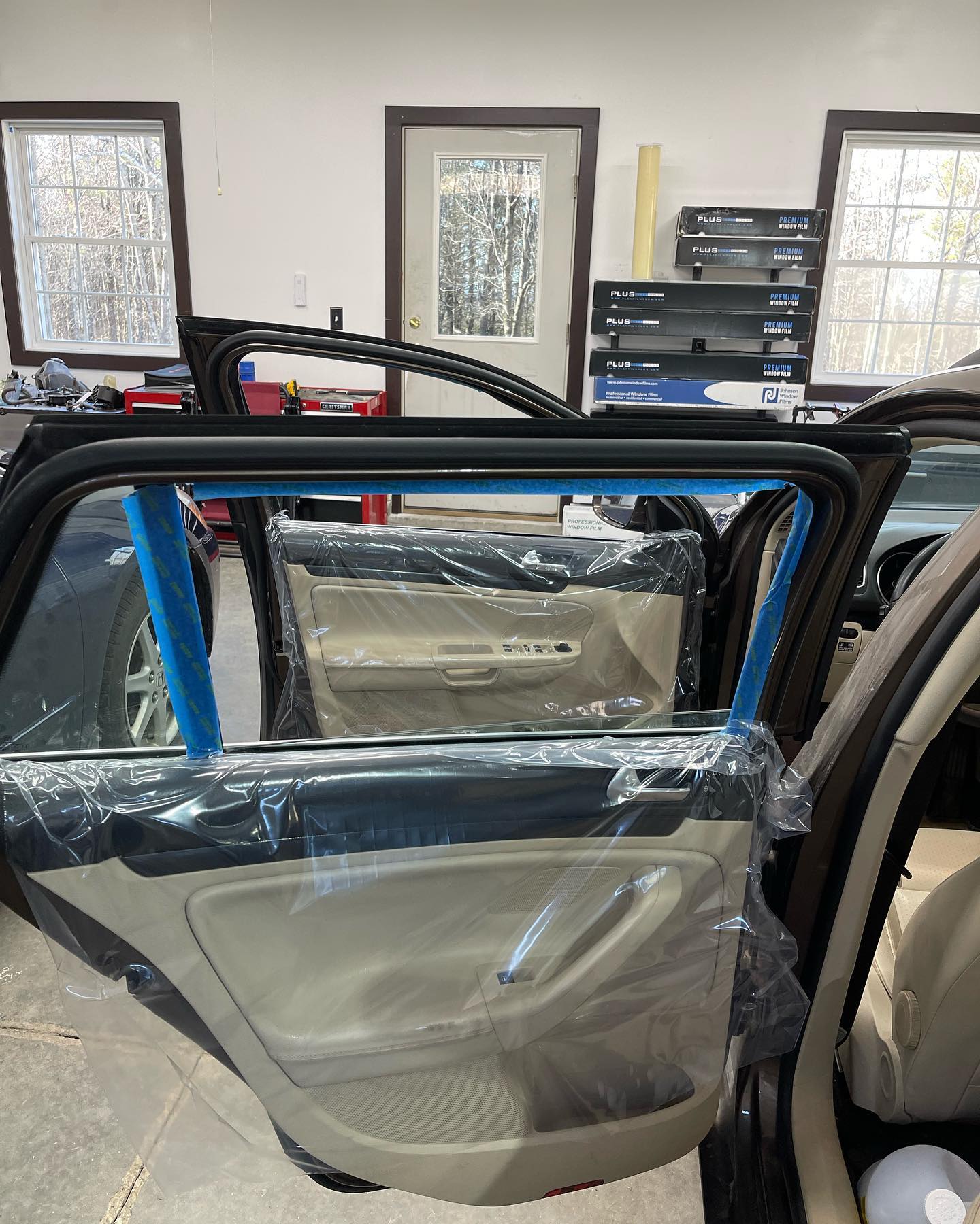 Car doors covered in plastic, likely for tinting, in a garage.