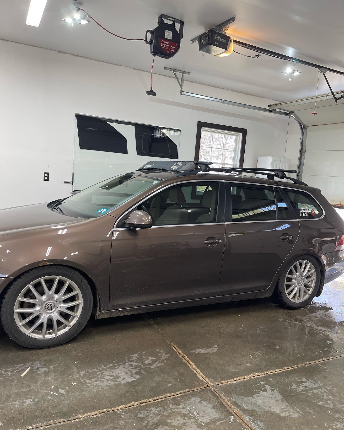 Brown station wagon parked in a garage, with roof rack. Garage door and opener visible.