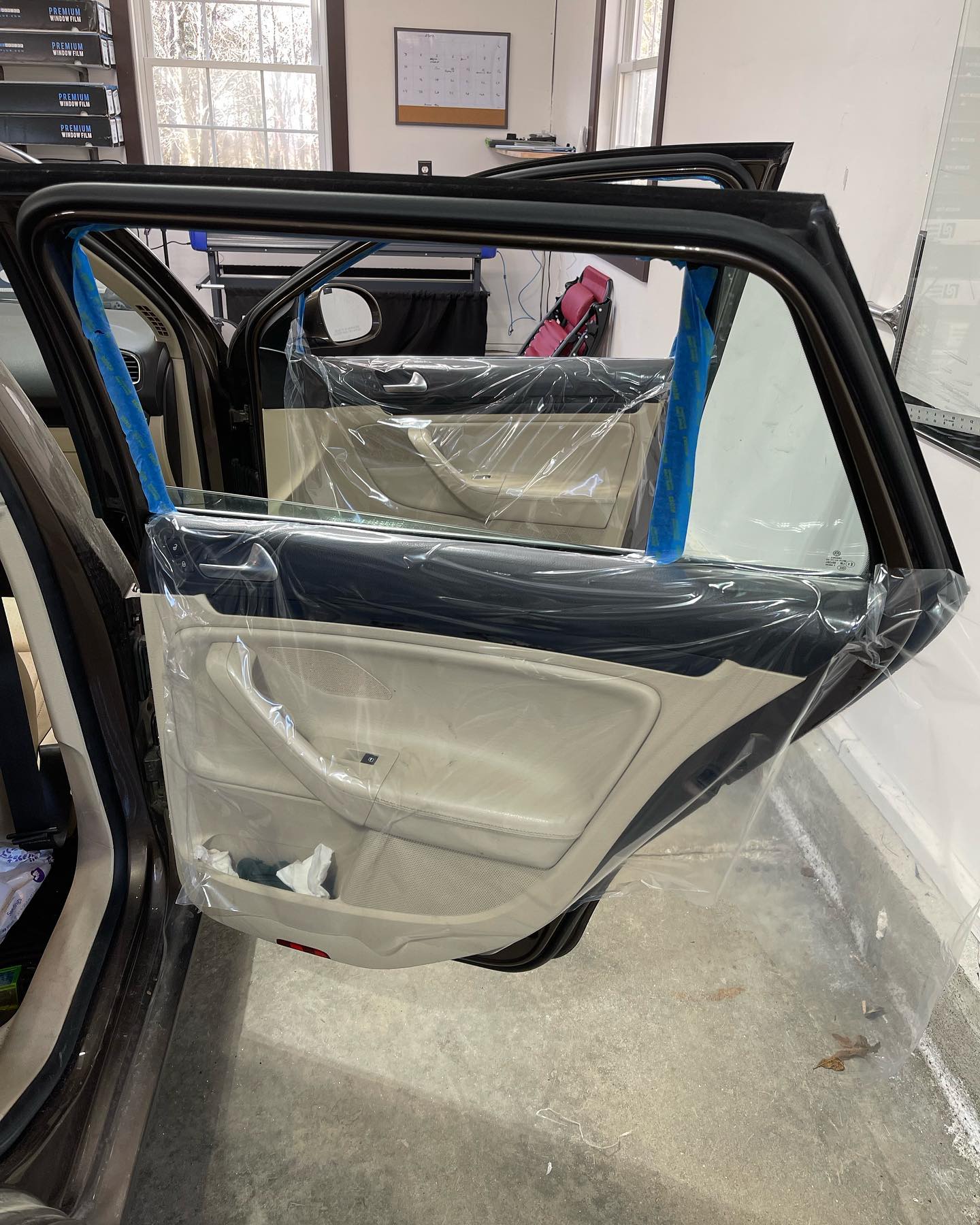 Car door with clear plastic wrap protecting interior. Open in a garage.
