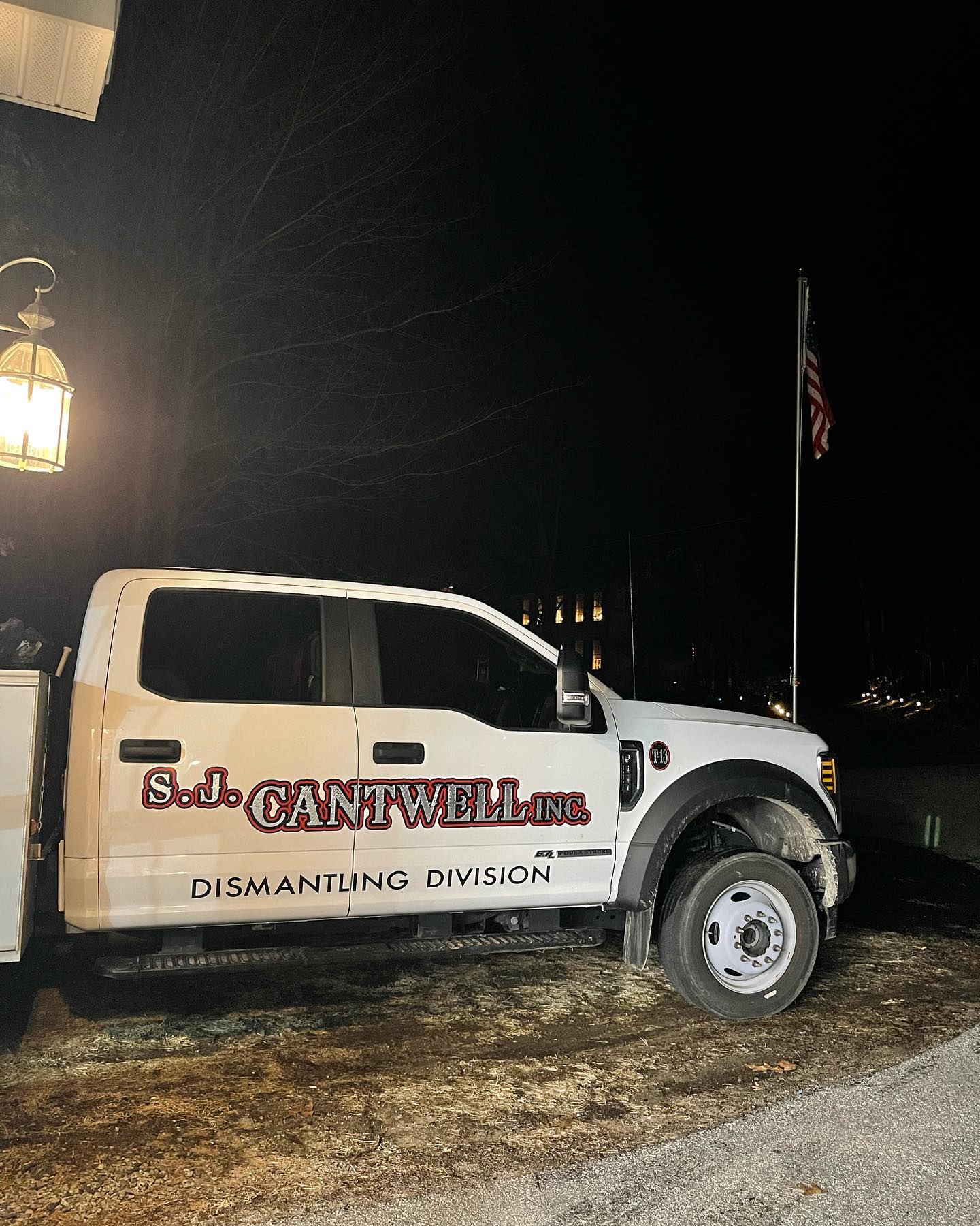 White S.D. Cantwell Inc. Dismantling Division truck parked outdoors at night, American flag in background.