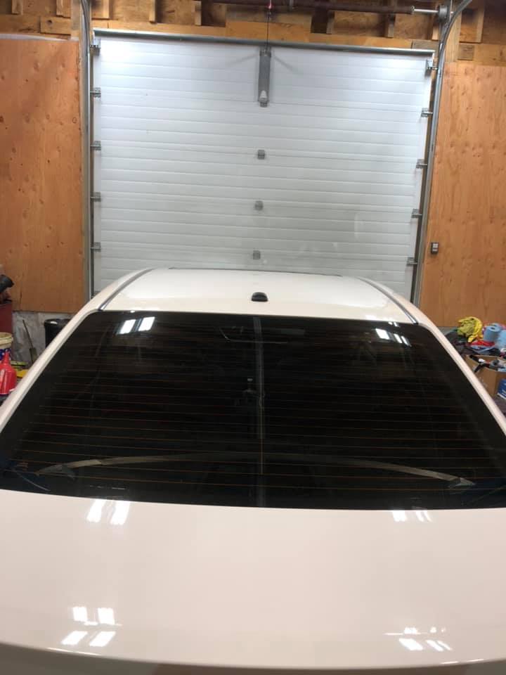 White car's rear with tinted window, garage door in background.