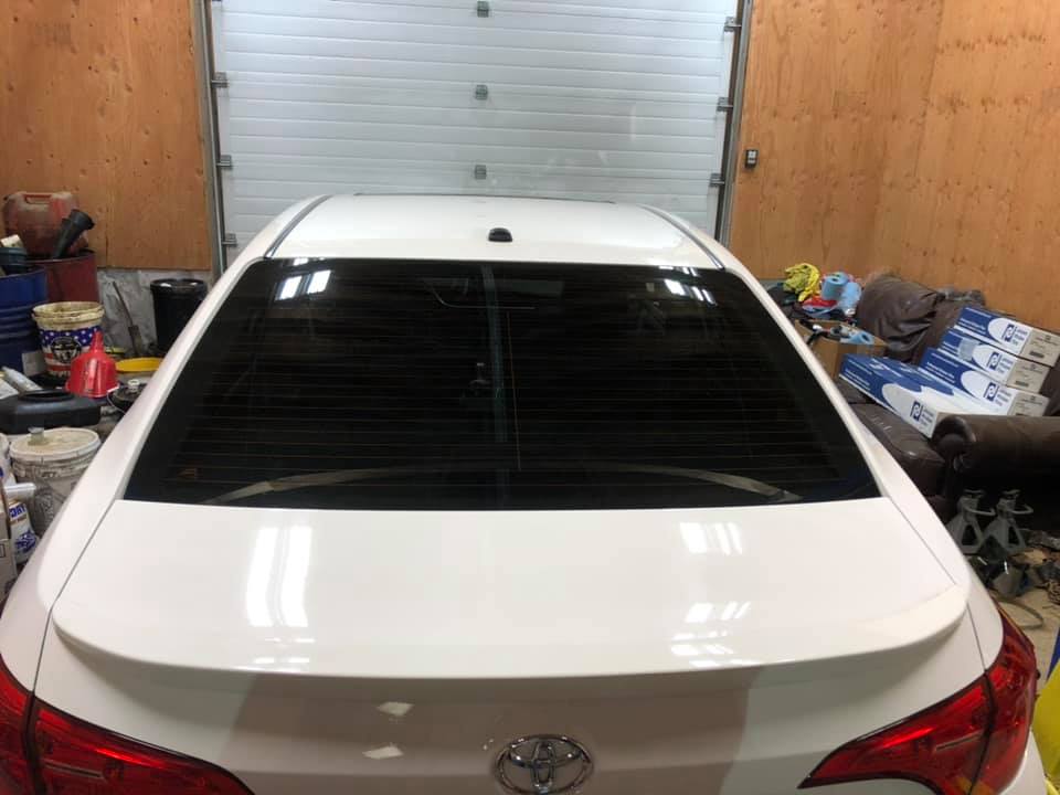 White car with tinted rear window, parked in a garage with a closed overhead door.
