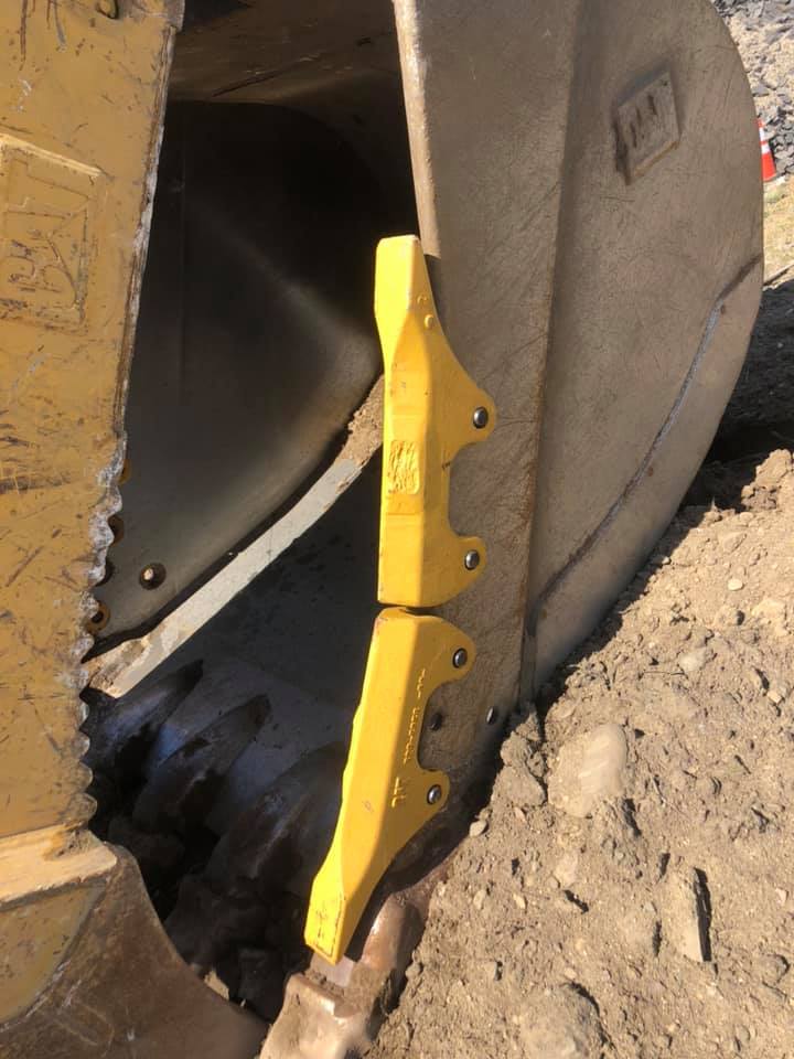 Yellow, pointed teeth on a construction machine bucket, digging into the earth.