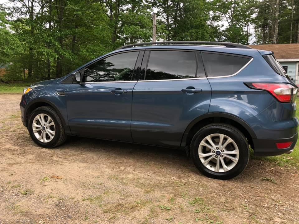 Blue SUV parked on a dirt surface with trees in the background.