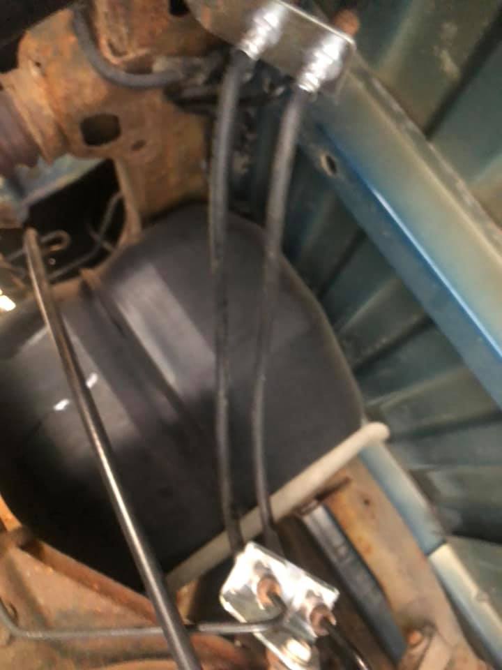 Underside view of a vehicle's black tank and hoses with a silver junction box attached to the frame.