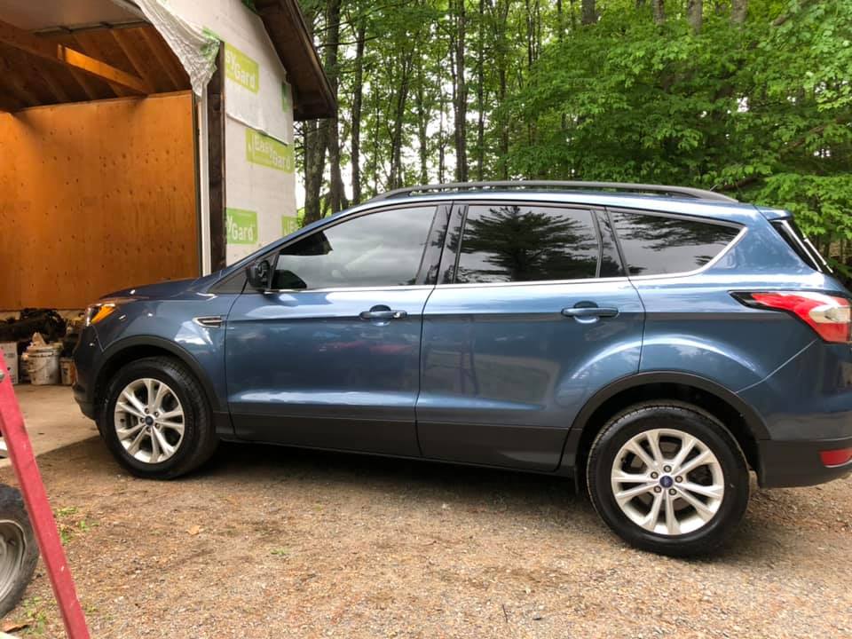 Blue Ford Escape SUV parked next to a building with trees in the background.