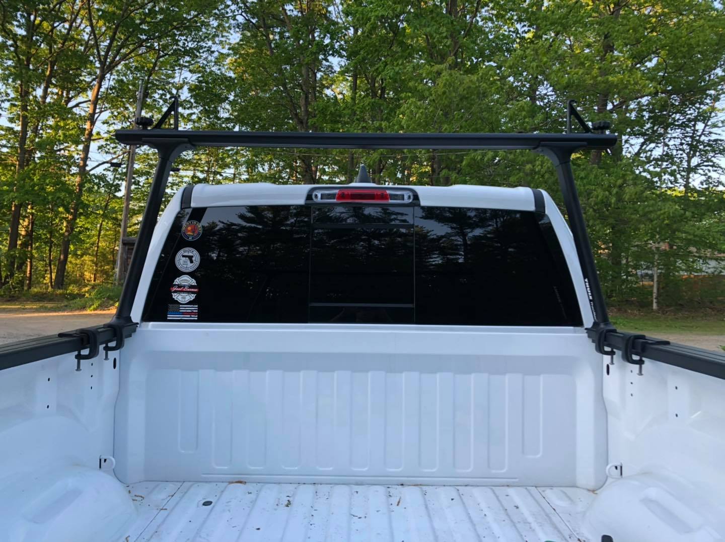 White pickup truck bed with a black ladder rack, trees in the background.