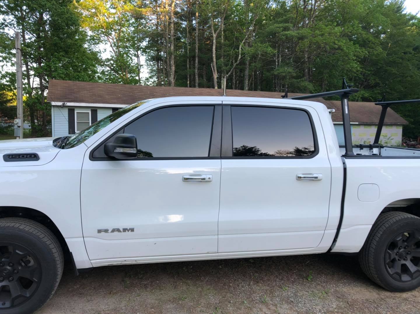 White Ram pickup truck with tinted windows and a black roof rack, parked in front of a house.