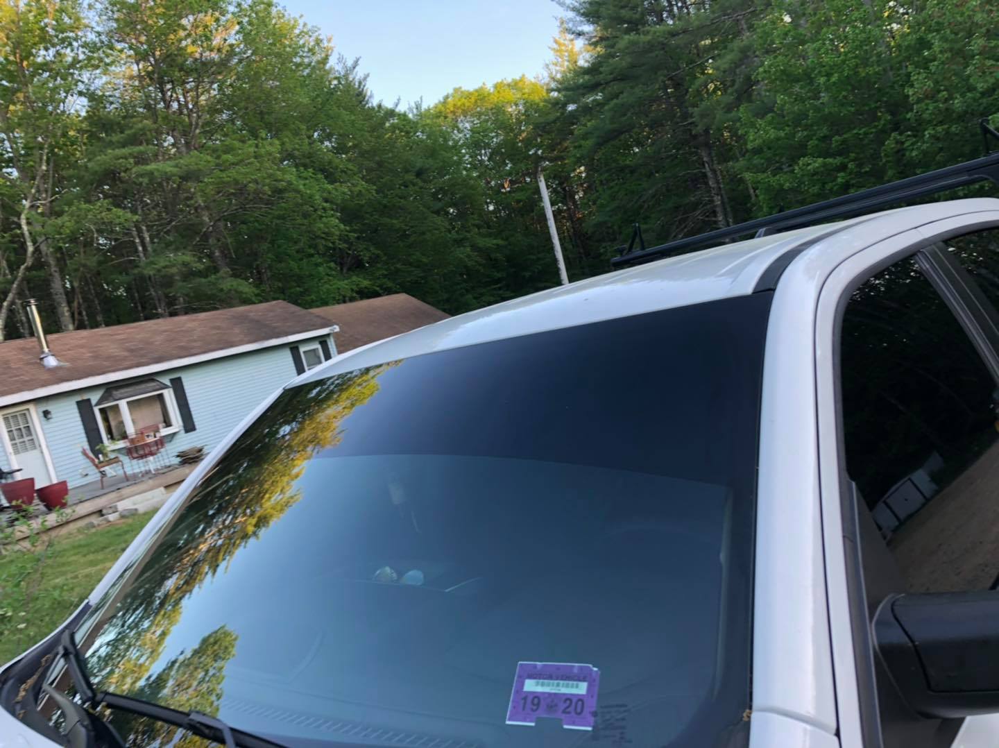 Close-up of a white SUV's windshield with dark tint. A house and trees are in the background.