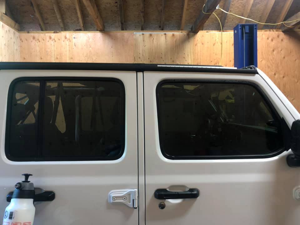 White Jeep door with tinted windows. A water bottle and blue container visible. Inside a garage.