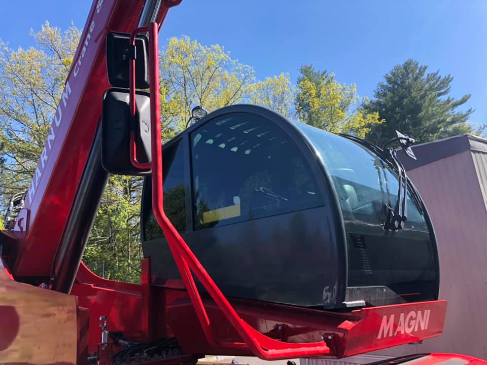 Red Magni telehandler cab, with tinted windows, parked outdoors.