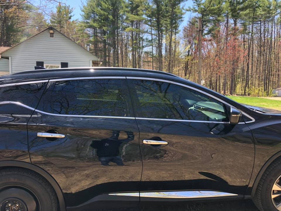 Black SUV parked in front of a white building with trees in the background on a sunny day.