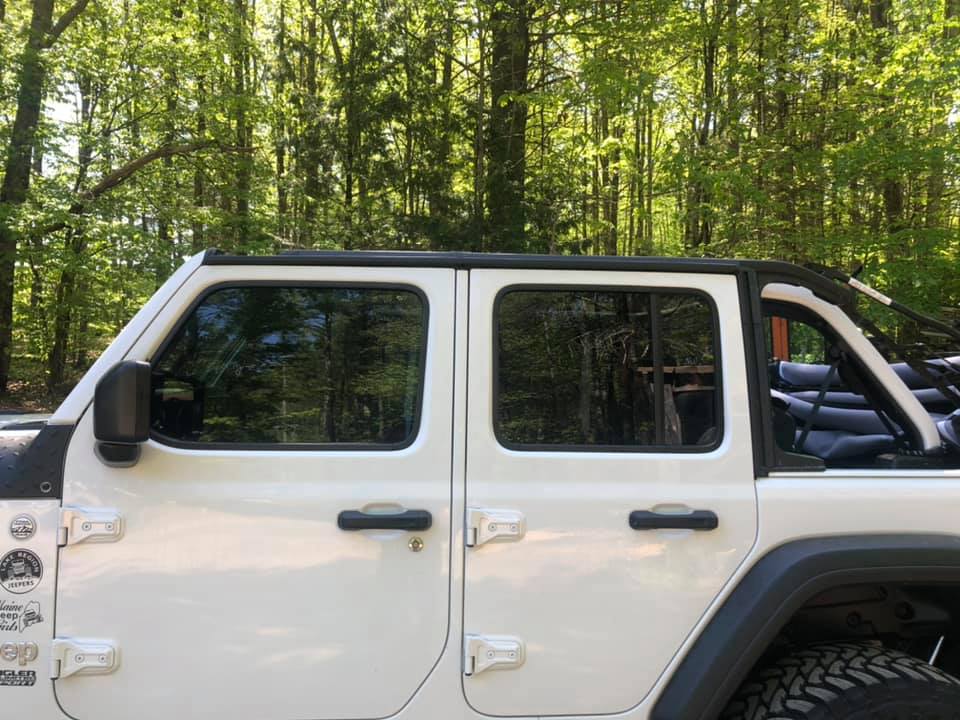 White Jeep side view with tinted windows, black roof, and forest background.