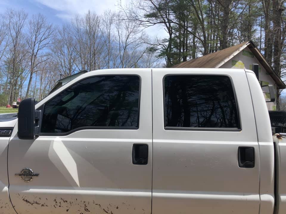 White pickup truck with tinted windows, parked outdoors near a house and trees.