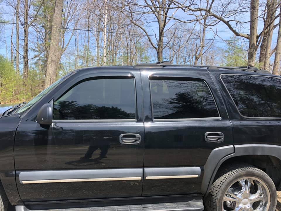 Black SUV with tinted windows parked near trees on a sunny day.