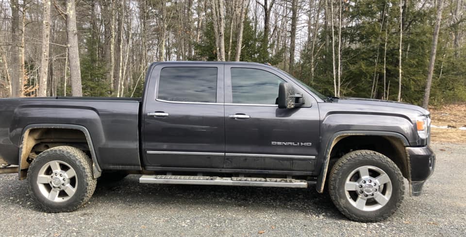 Dark gray GMC truck parked on a gravel road, forest in the background.