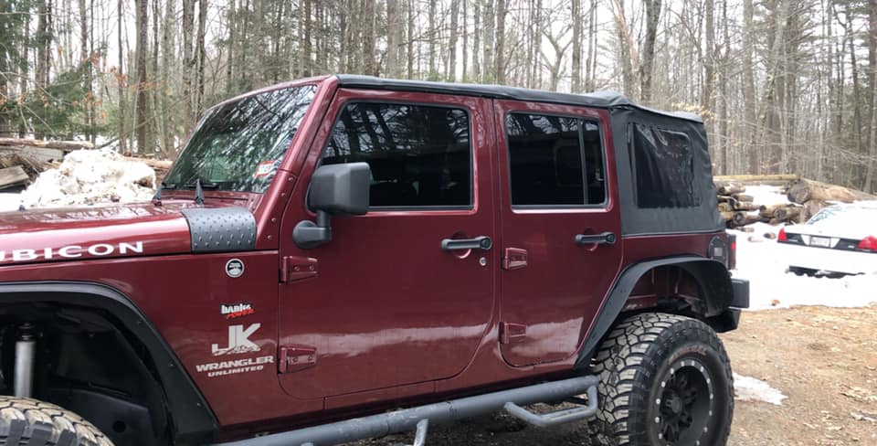 Red Jeep Wrangler Rubicon with black soft top, parked outdoors with snow on the ground.