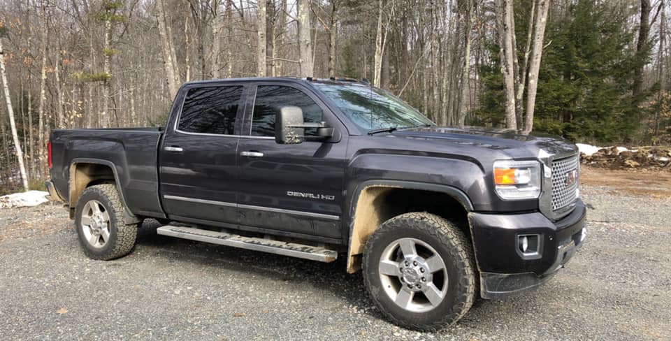 Dark grey GMC pickup truck parked on gravel road with trees in the background.