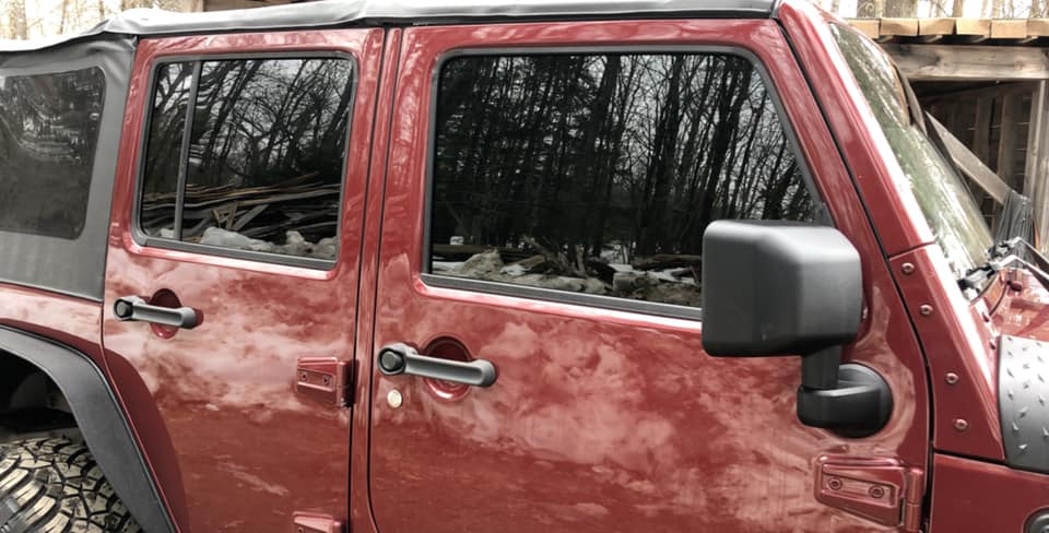 Red Jeep Wrangler with tinted windows and black side mirror.