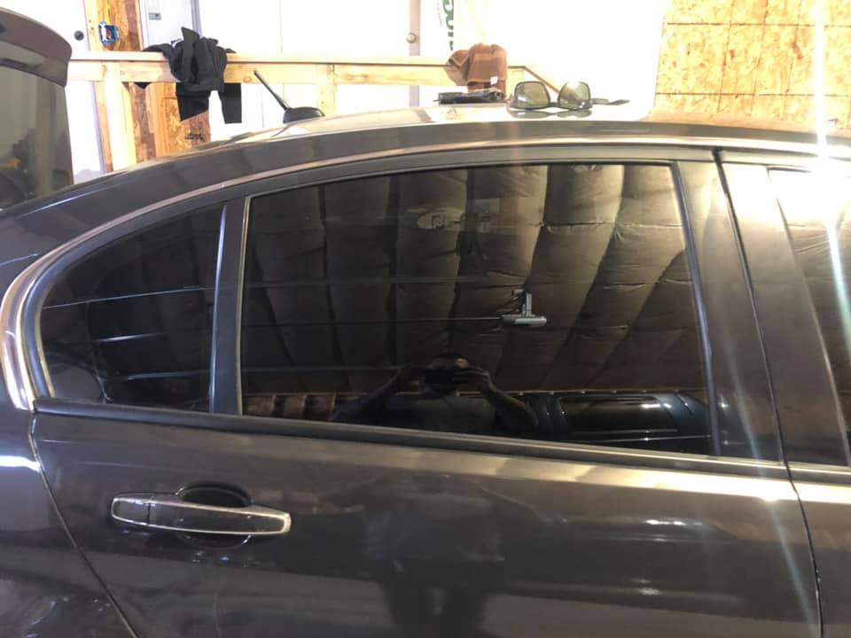 Dark gray car with a window repair in progress, inside a workshop.
