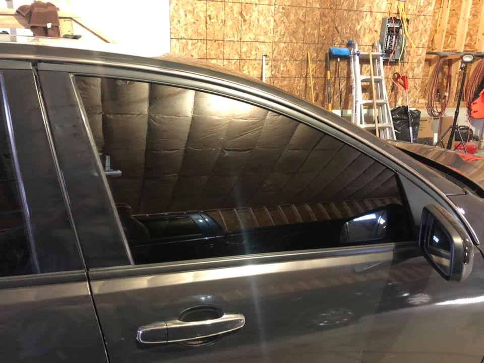 Gray car parked inside a garage. The windows are tinted, reflecting the interior.