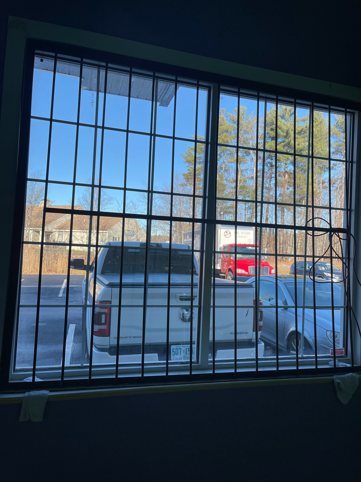 Window with security bars, looking out at a parking lot with cars and a clear, blue sky.
