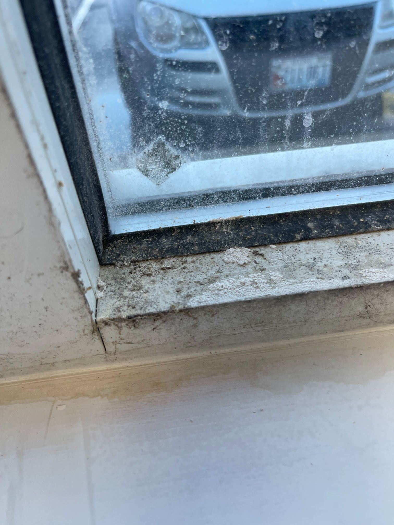 Close-up of a window frame with dirty glass, showing a car's reflection and a visible diamond-shaped mark.