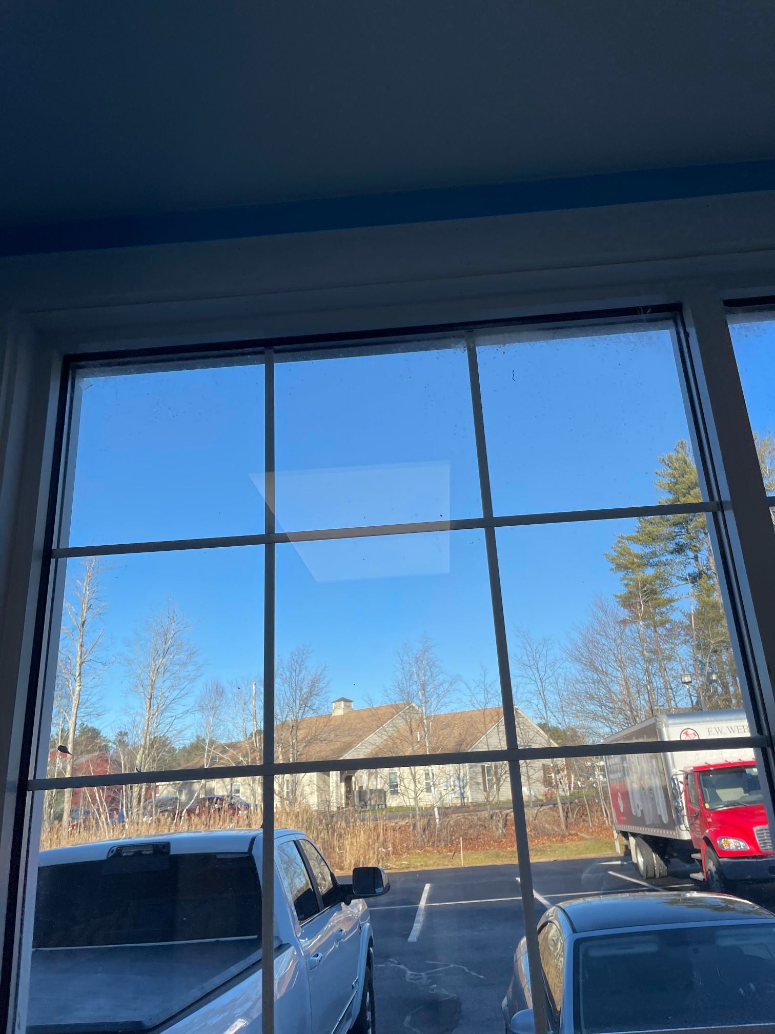 Large window with a grid view overlooking a parking lot, houses, and a blue sky.
