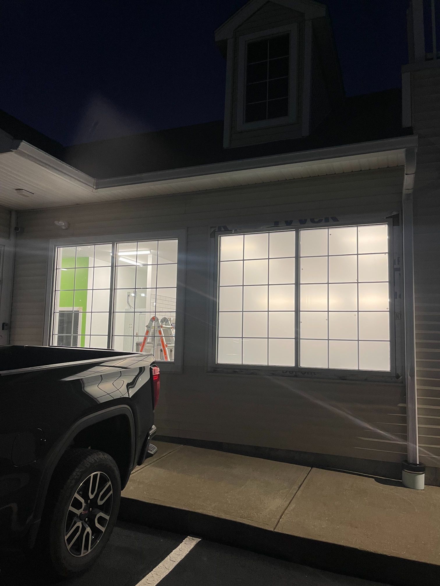 Dark exterior shot of a building with glowing square windows; a truck is parked in front.