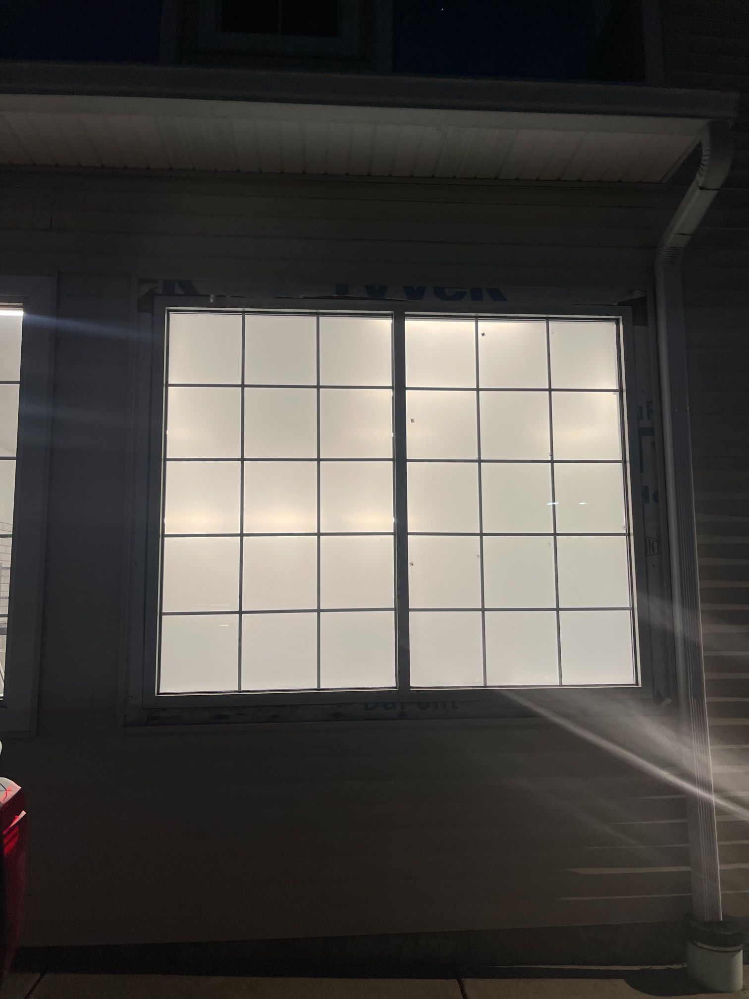 Window with a grid pattern, light shining through. Exterior shot at night.