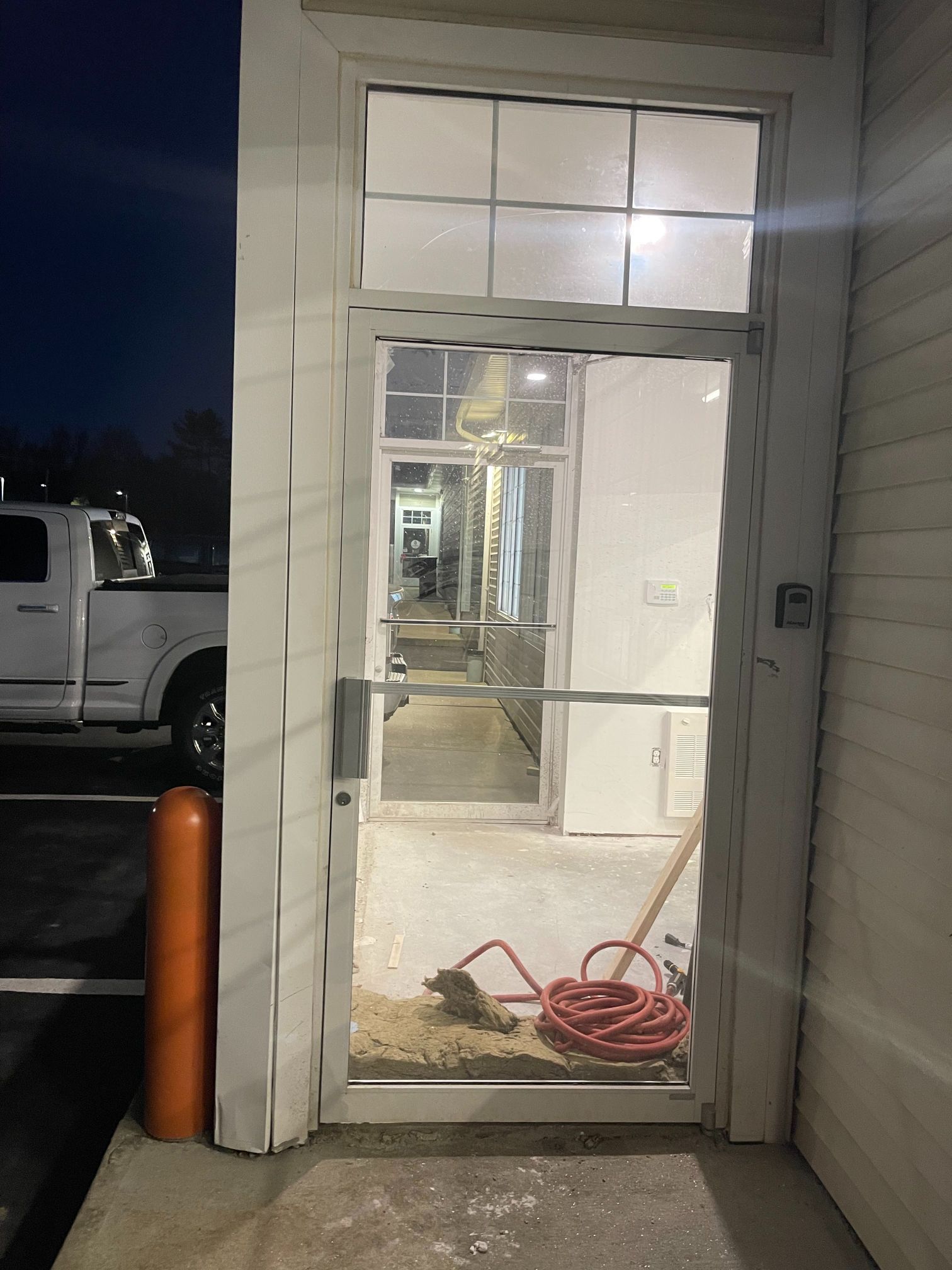 White entry door with a view into a building under construction; a red hose and broom are visible.