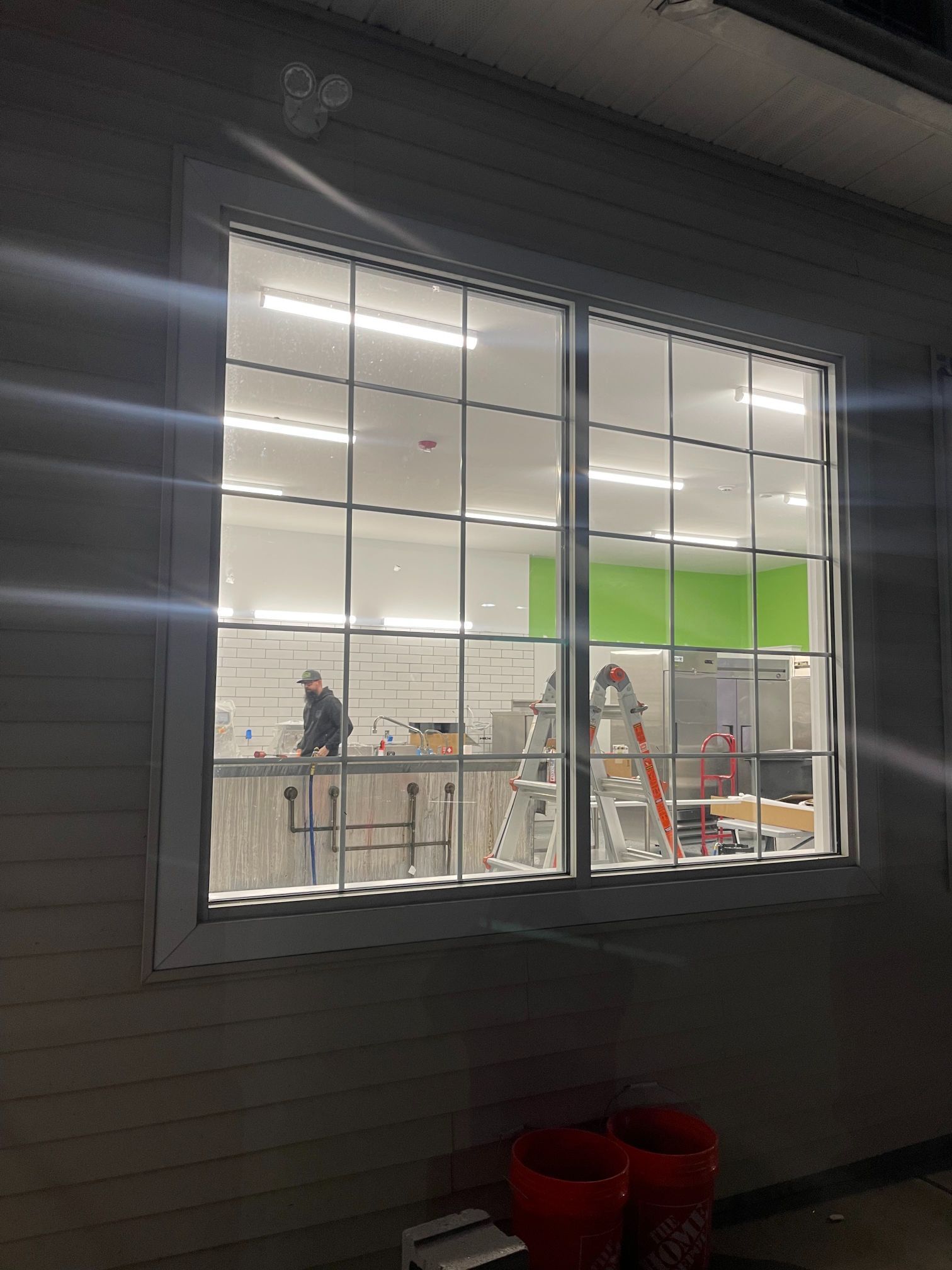 Exterior view of a window with grid pattern, inside a brightly lit room with a person and construction equipment.
