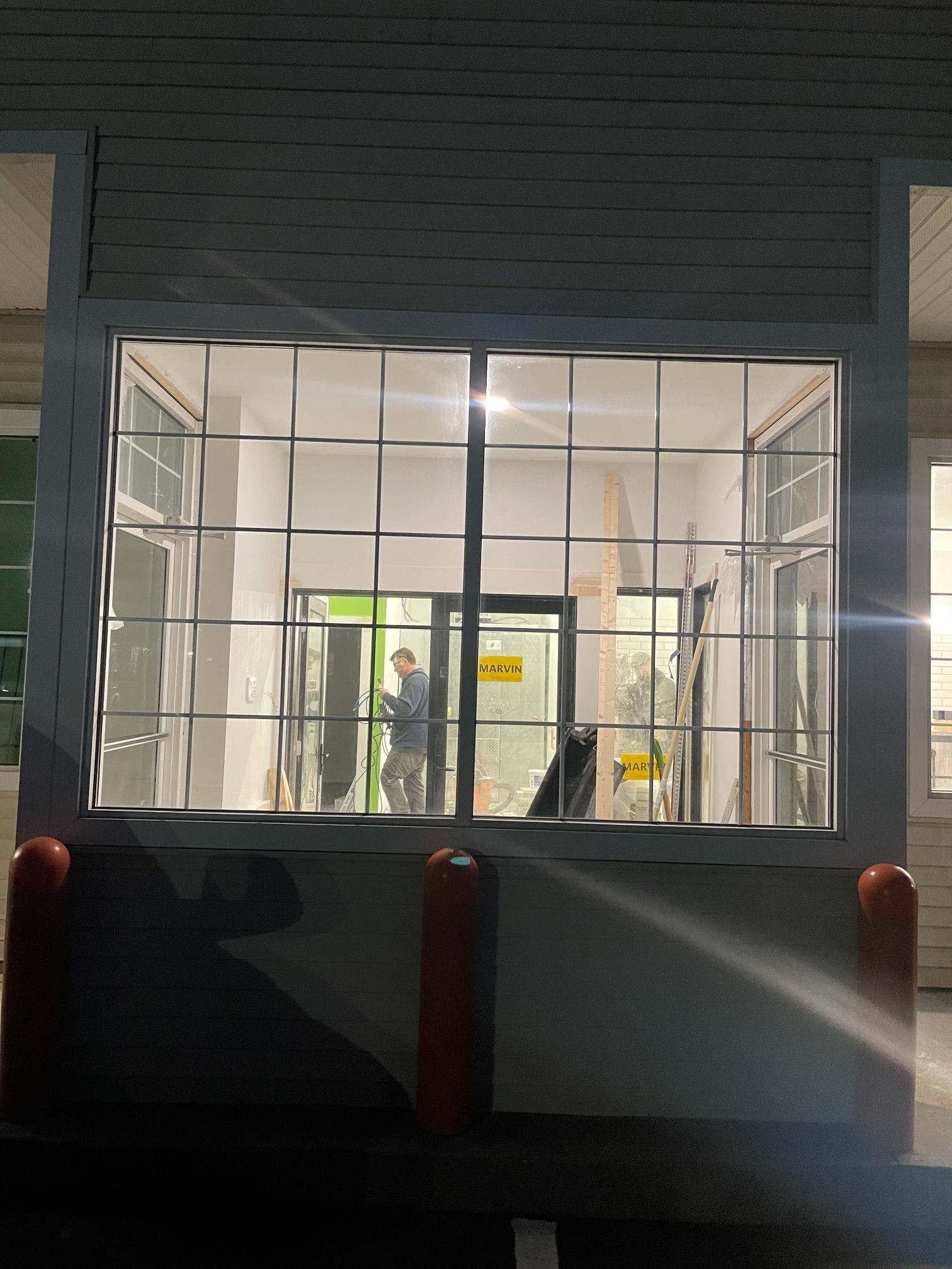 Exterior nighttime shot of a building window. A person inside, with a dog. Gridded window panes. White walls.