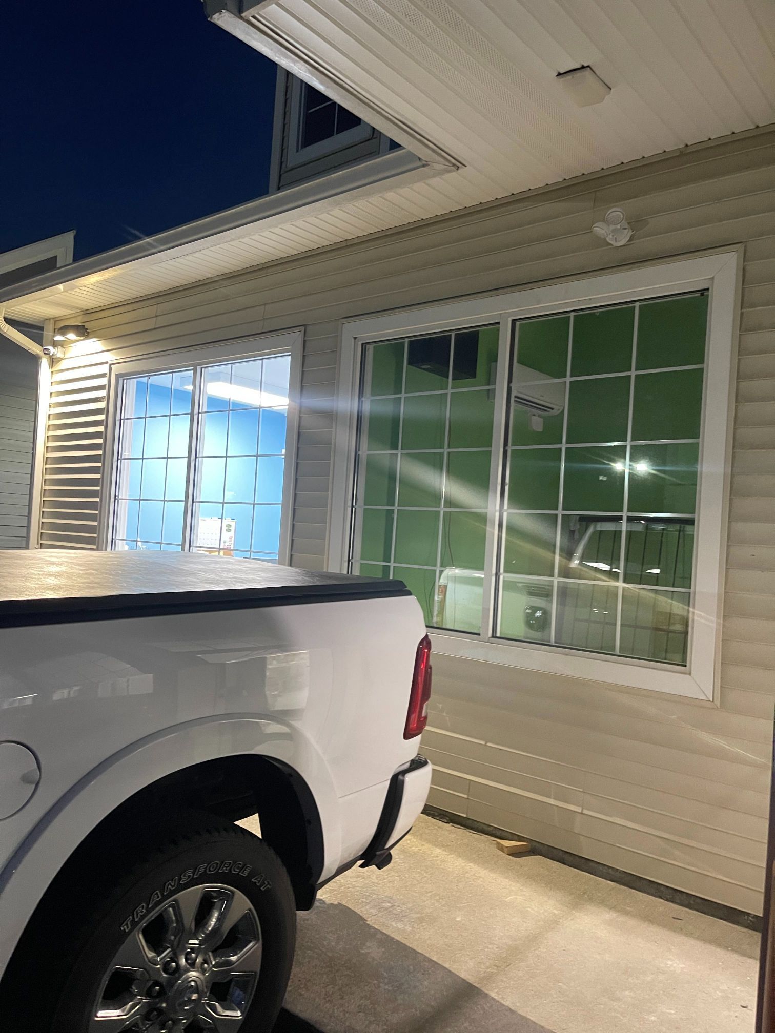 White truck parked next to a building with two windows. The left window is open, revealing a blue interior