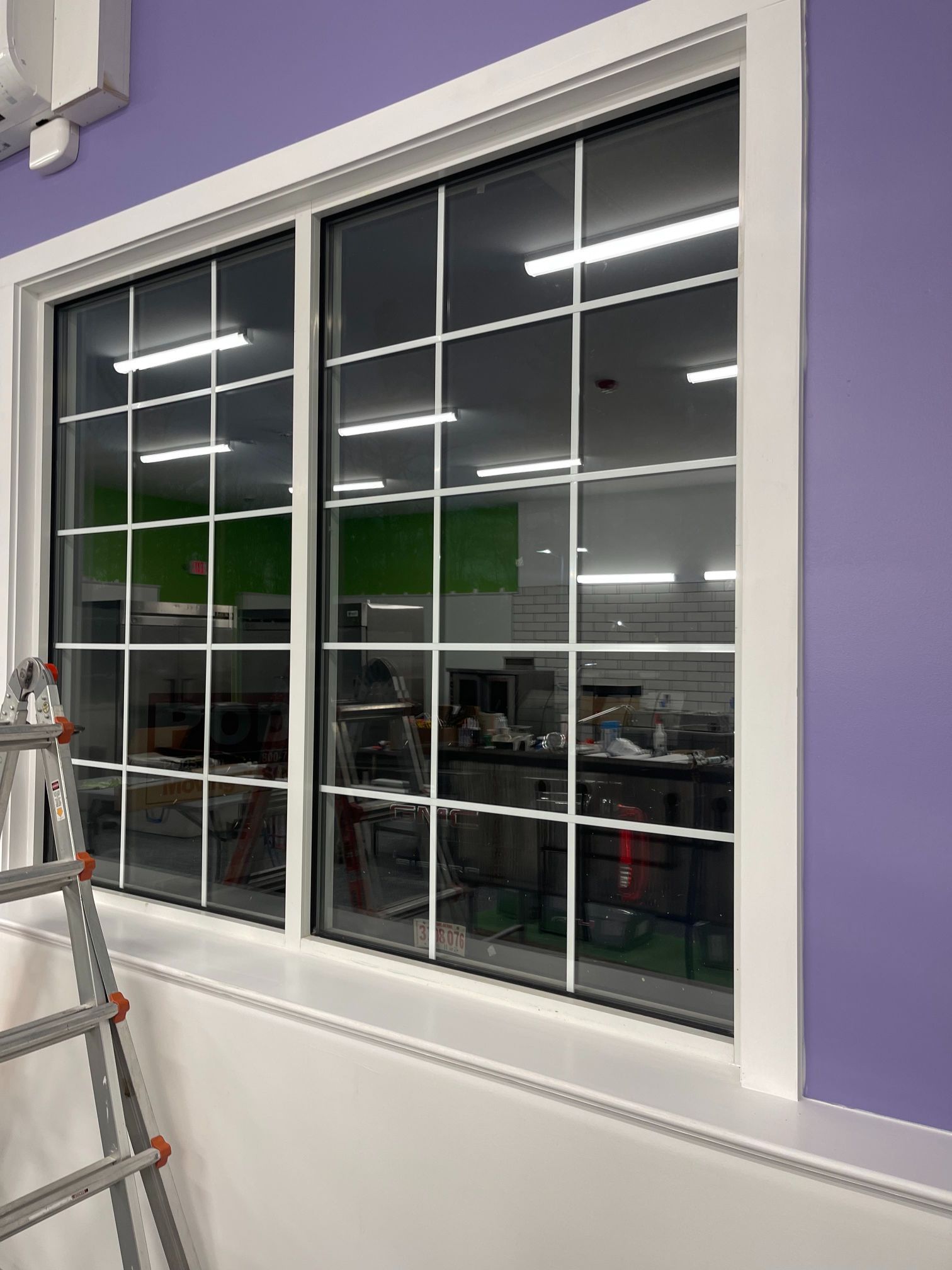 White-framed window with grid pattern, set in purple wall. Silver ladder leans against the left side.