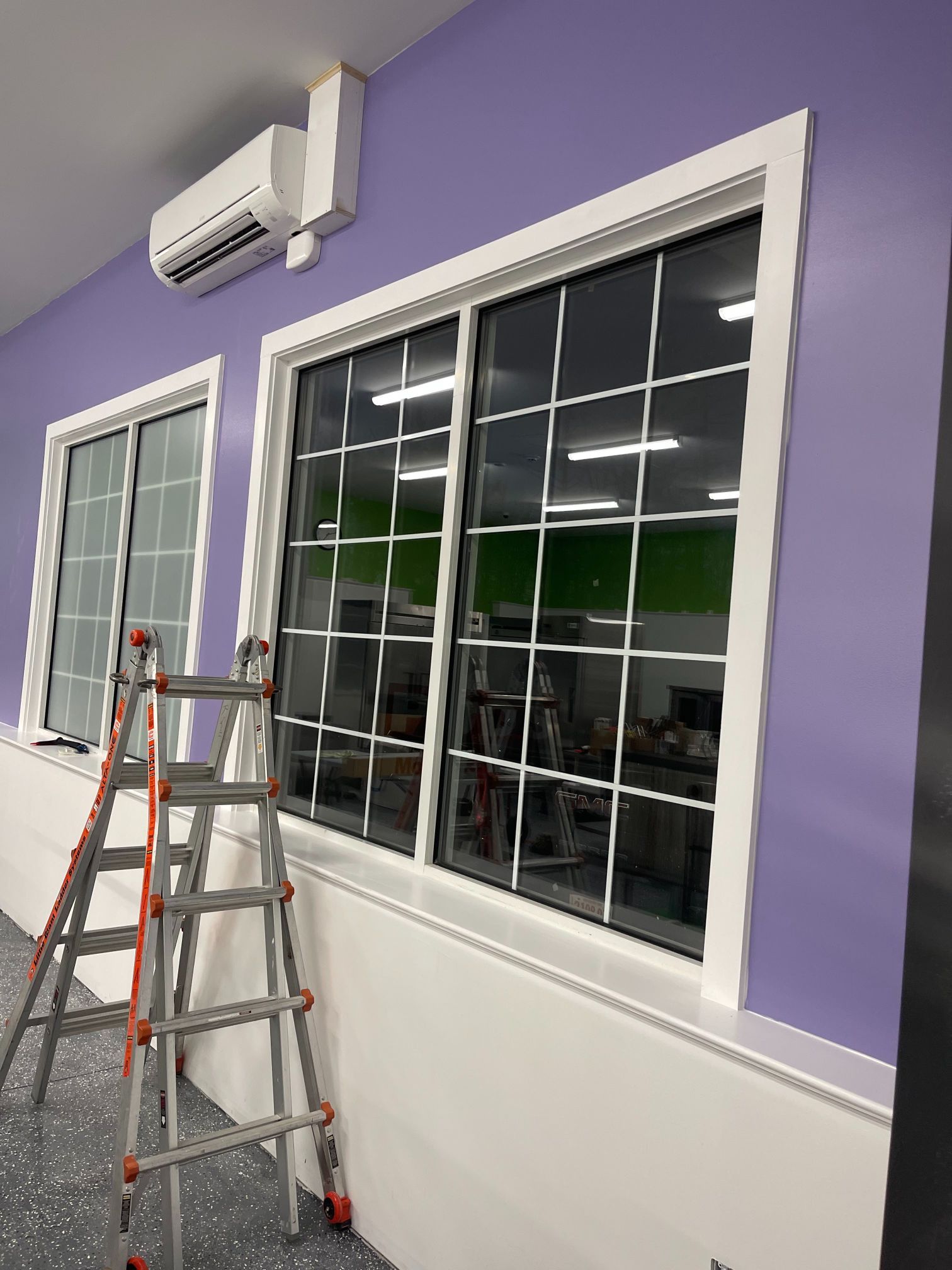 Two white-framed windows with grid patterns on a lavender wall. A ladder is in front of the window.