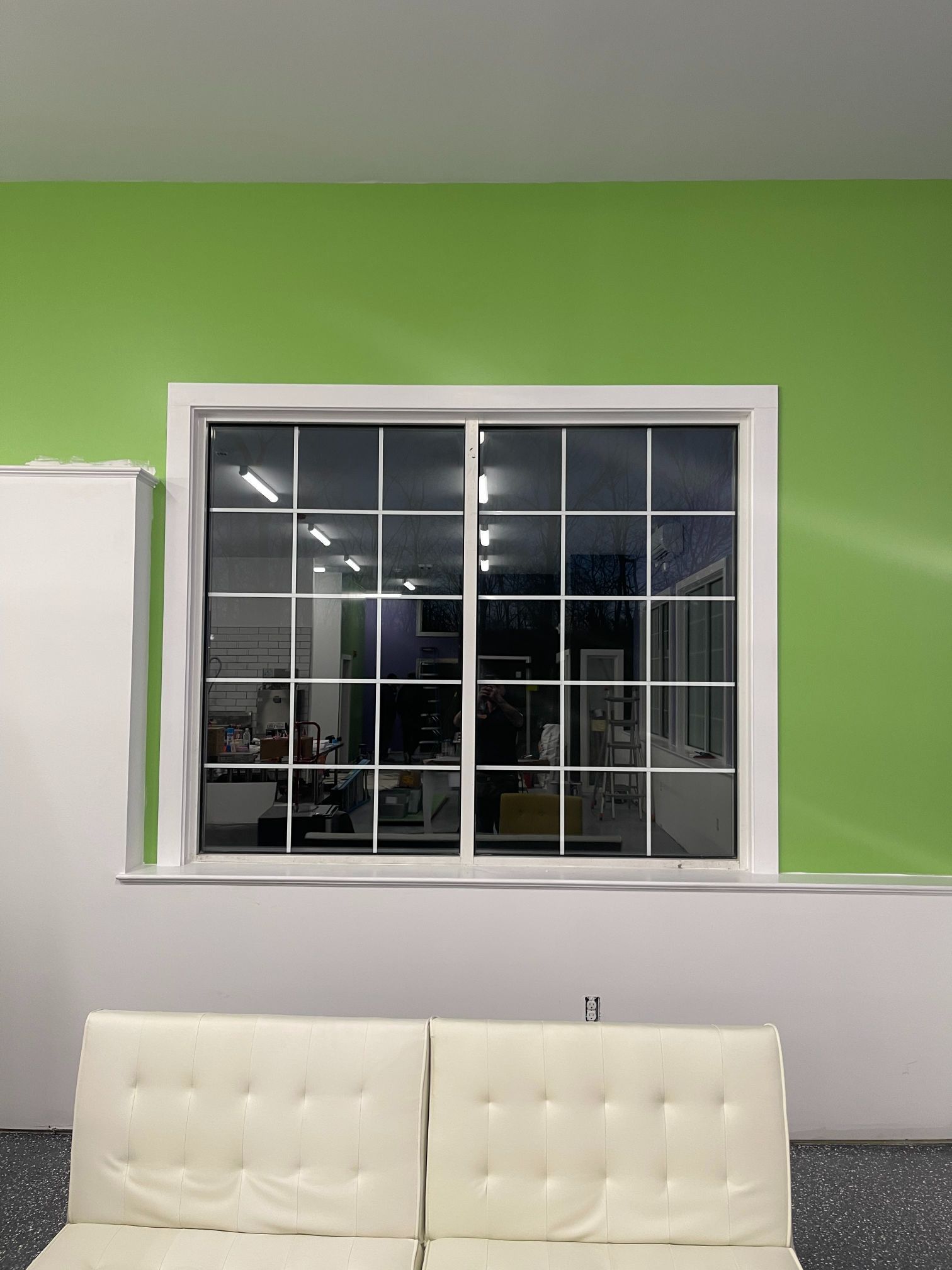Window with white grid in a room with green and white walls, white sofa.