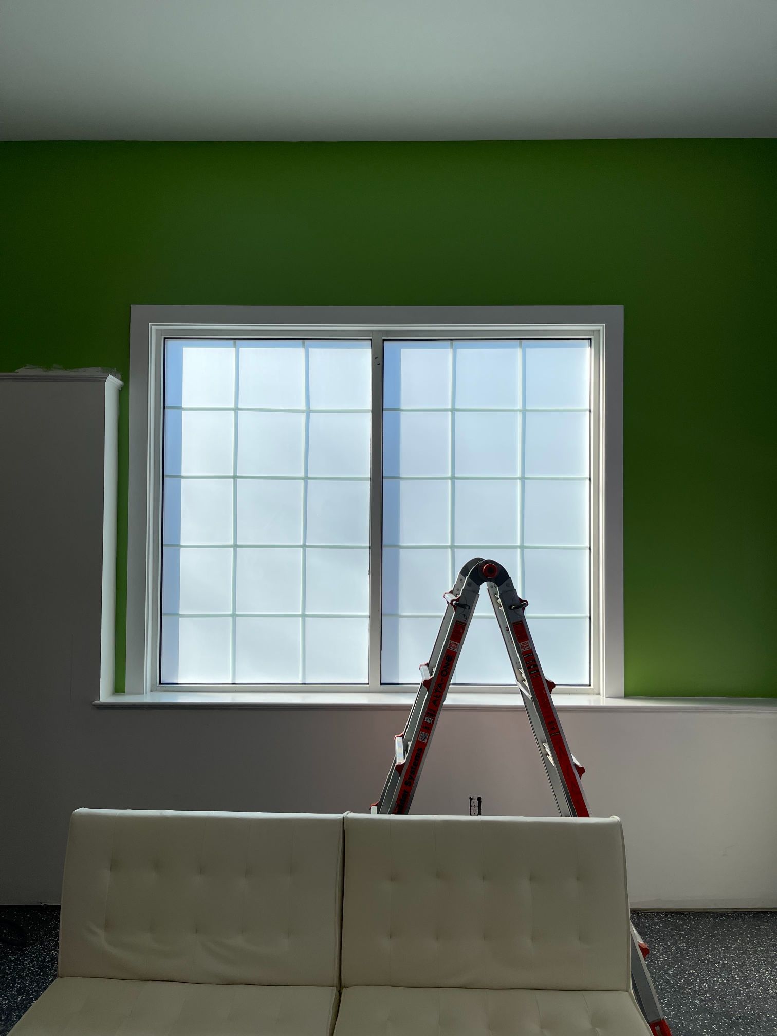 Ladder against window in room with green walls. White couch in foreground.