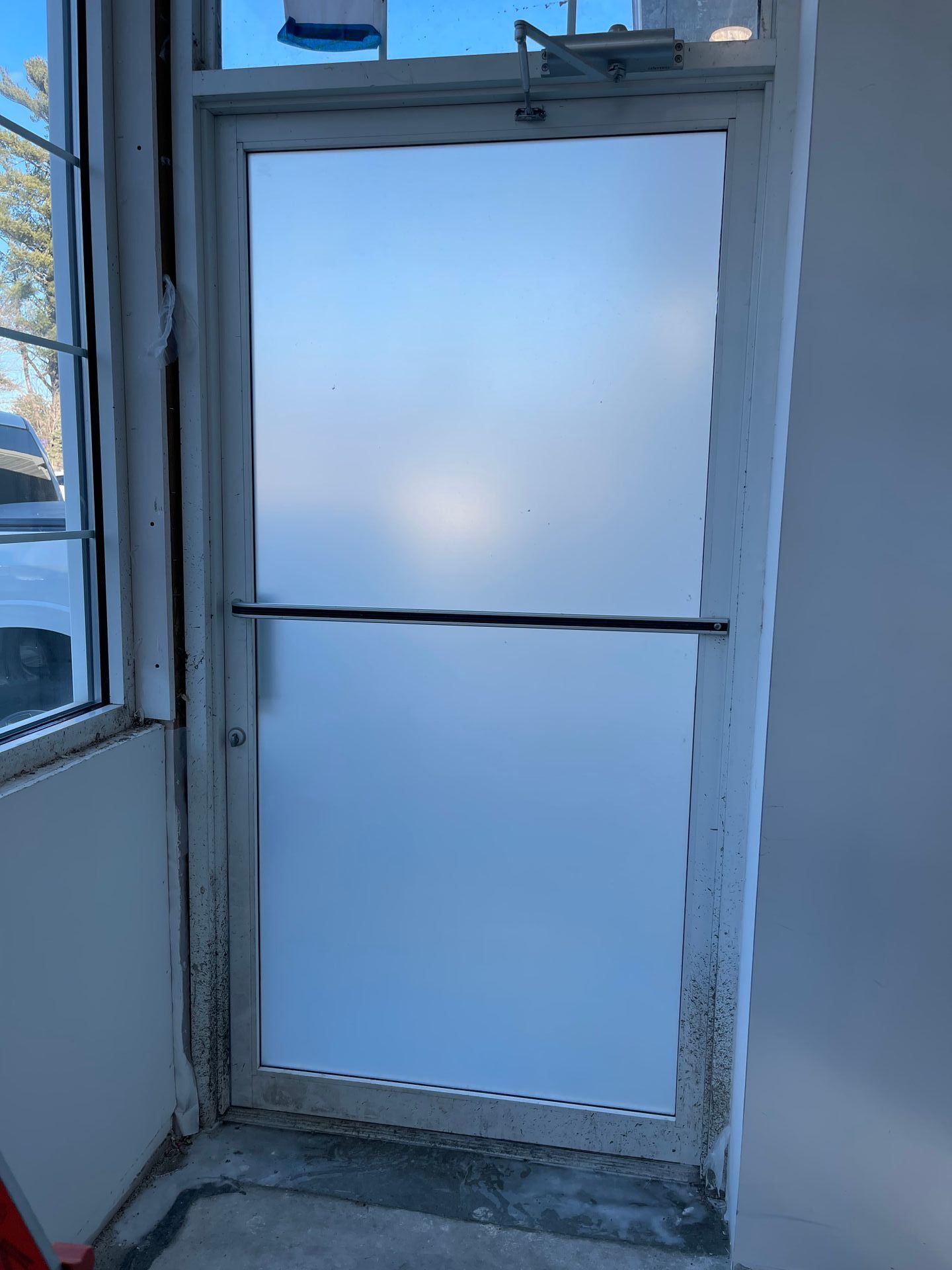 Frosted glass door with a horizontal bar, in a white frame, in a building entrance.