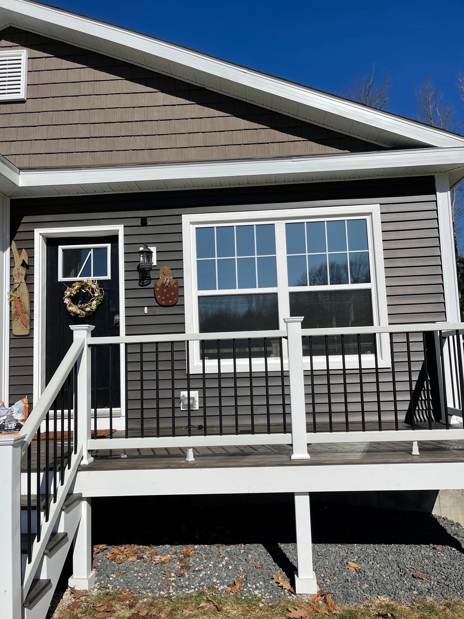 Gray house with white trim, front porch, black door, and a window.