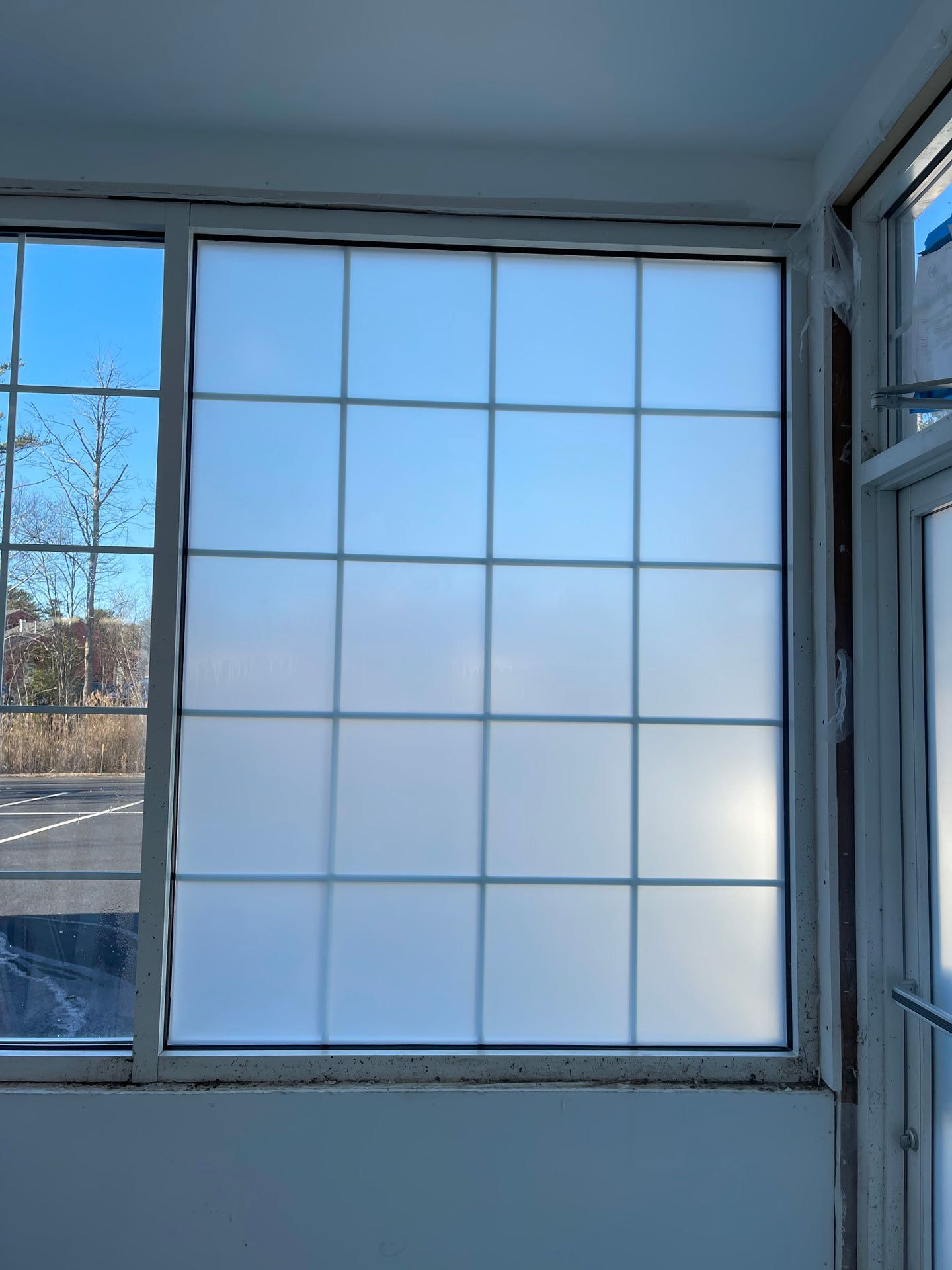 Large, grid-patterned window with frosted glass reflecting a clear sky. A smaller window is to the left.